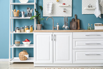 Wooden counter with silver sink, pegboards and shelving unit near blue wall in kitchen