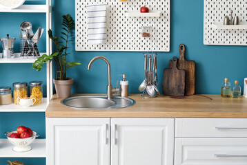 Wooden counter with silver sink, pegboards and shelving unit near blue wall in kitchen