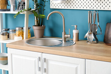 Wooden counter with silver sink, cookware, houseplant and dish soap near blue wall in kitchen