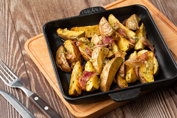 Delicious Fried Potato Bratkartoffeln With Bacon and Onion close up in the black plate on the table.