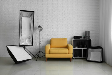 Comfortable armchair and different equipment near white brick wall in modern photo studio interior
