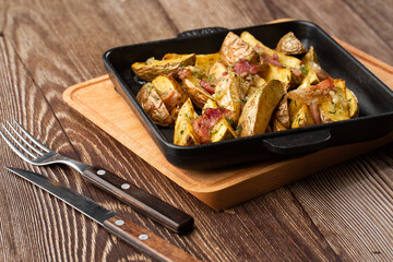 Delicious Fried Potato Bratkartoffeln With Bacon and Onion close up in the black plate on the table.