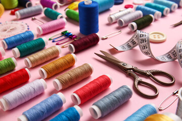 Thread spools, scissors and measuring tape on pink background