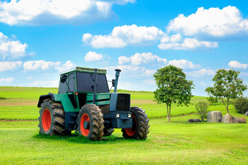 A green tractor is parked on a lawn and behind it is a beautiful cloudy sky. Concept. Antique tractor with beautiful garden decorations.