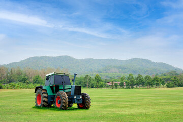 Fototapeta premium A green tractor is parked on a lawn and behind it is a beautiful cloudy sky. Concept. Antique tractor with beautiful garden decorations.