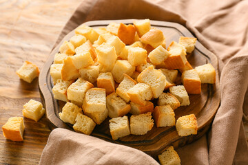 Board with tasty croutons and napkin on wooden background, closeup