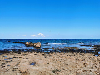 Fototapeta premium The coast of the Mediterranean Sea, waves, clear water, a stone ridge against a blue sky with clouds.