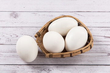 Fresh goose eggs in a rattan basket on wooden table