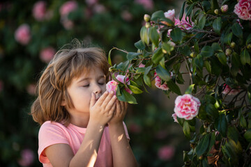 Charming blond child on background of flowers in summer. Pretty little child working in garden,...