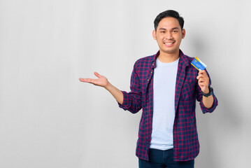 Smiling young Asian man in plaid shirt showing credit card, present blank space in hand isolated on white background