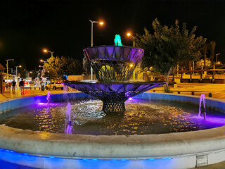 Overnight in Cyprus in Protaras. A purple-lit fountain on a central street against a dark sky.