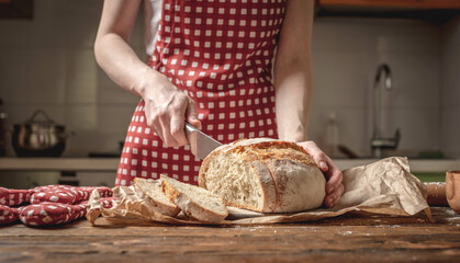 Hands cut with a knife homemade natural fresh bread with a Golden crust on wooden background. Baking bakery products