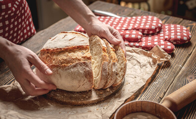 Hands cut with a knife homemade natural fresh bread with a Golden crust on wooden background. Baking bakery products