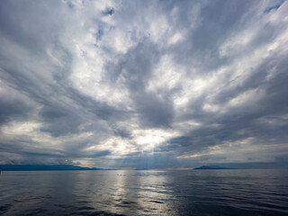 The silence before the storm. Sun beams falling from grey clouds. Moody sky and mountain view from sea perspective. Beautiful natural background with large space for copy space.