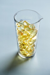 Capsules of omega-3 fatty acids on a blue background in a glass. The concept of medicine and a healthy lifestyle. Vertical photo.