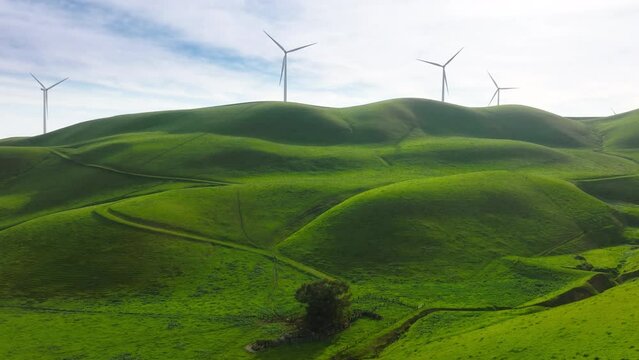 Windmill park green source of energy, windmill wind farm on green hills with rotating windmill turbine blades generating renewable energy from wind. 4k cinematic aerial California countryside USA