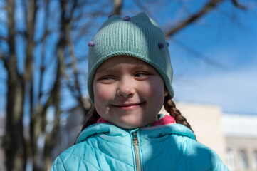 A portrait of a happy Ukrainian girl against the blue sky and trees. A five-year-old child smiles a sly smile as she looks past the camera. Spring time. City park.