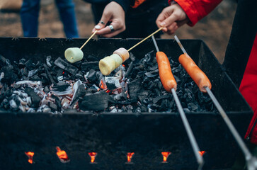 Cooking on coals. Marshmallows are fried on coals. Sausages on skewers. Women's hands cook food in a barbecue in nature. A fire on charcoal.