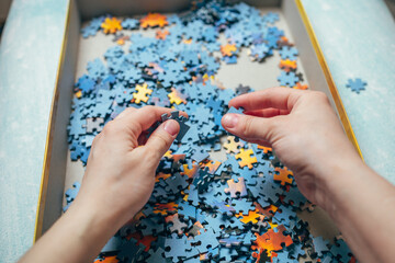 Women's hands hold pieces of puzzles. Cardboard box with puzzles. Hobby, board game.
