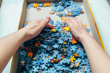 Women's hands put together pieces of puzzles in a cardboard box. Hands are raking puzzles.