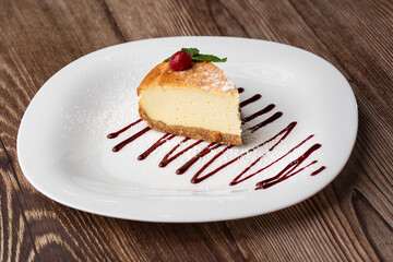 Cheesecake New York or classic cheesecake with caramel. Closeup view. Tasty breakfast. Piece of cake on white plate, on wooden background.
