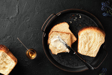 Sweet brioche bread on tray with knife , butter and honey on a dark vintage surface. Flat lay traditional sweet French brioche, baked concept.