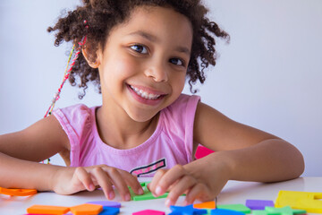 Beautiful latin mixed race girl smiling at camera while playing with colorful educational toys on...
