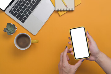 Above view woman hand using mobile phone on yellow background. Empty screen for graphic display montage.