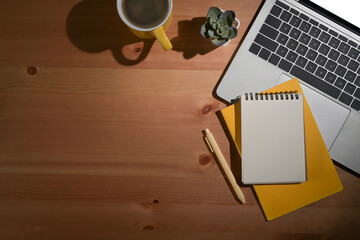 Wooden table with computer laptop, coffee cup and notebook. Top view, copy space.