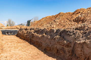 Dig a trench. Earthworks, digging trench. Long earthen trench dug to lay pipe or optical fiber. Construction the sewage and drainage. View from the trench. Clay soil. Part of the image is blurred.