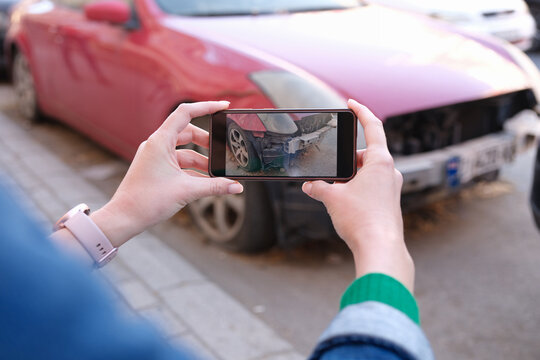 Woman holding smartphone and taking picture of car accident