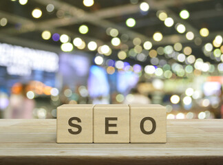 SEO letter on wood block cubes on wooden table over blur light and shadow of shopping mall,...