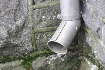 Metal drain pipe next to stone wall