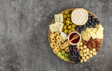 Top view of a tasty cheese plate with grapes, honey, nuts, olives, and cheese varieties on a wooden...