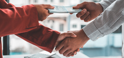 Shaking hands with congratulations on an evil plan, Businessmen give dollars to bribe employees in signing contracts to buy illegal land and real estate, corruption and Bribery concept.