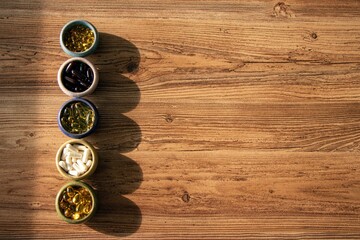 several types of dietary supplements in small plates on a wooden background with hard sunlight.