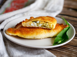 Baked patties or pies with ramson wild garlic, eggs and cheese. Homemade food. curd dough. Baking on a plate on wooden table with textile napkin, close-up. Local food