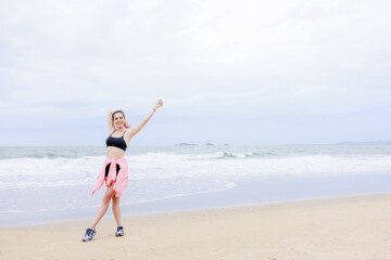 asian woman wearing sportwear and pink jacket exercise and relax on the sea beach at evening in the rain season