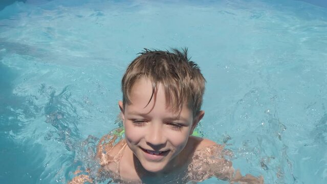 Smiling boy swims towards the camera, Caucasian child looking and smile into Camera