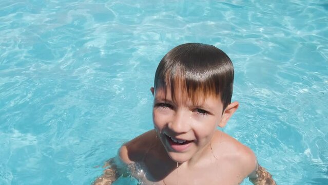 Caucasian boy emerges from pool water, happy kid looking into camera. summer Concept