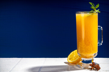 Traditional autumn hot honey sea buckthorn tea. Spicy fruity berry cocktail. Fall winter hot alcohol drink in warm cocktail glass, dark blue and white background, copy space