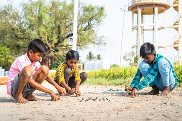 Indian village kids playing goli or marbles on near paddy field - concept of traditional game, summer holidays and leisure activities.