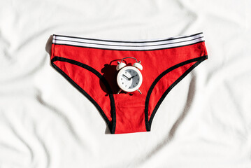Women's red underwear and alarm clock. Concept of women's health, menopause and critical days, abdominal pain. Menstrual cycle, gynecology, pregnancy. hormonal therapy - obrazy, fototapety, plakaty