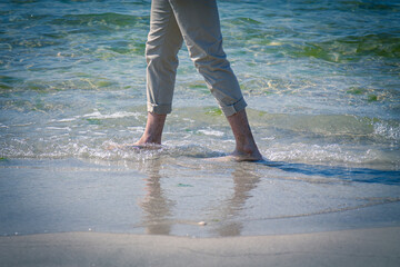 closeup of the bare feet of a man walking on the beach, on the edge of the waves foaming