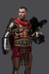 Portrait of naked gladiator champion with plumed helmet dressed in light armor isolated on grey.