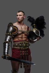 Shot of legendary roman warrior with muscular build holding gladius and plumed helmet.