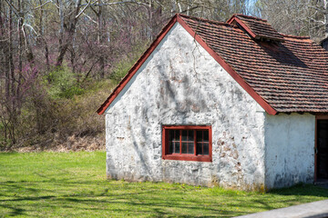 Side view of an white stone cottage with antique red window in rural landscape