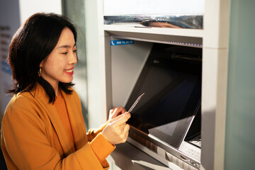 Happy smiling young woman withdrawing money from credit card. Young woman typing pin code on keypad...