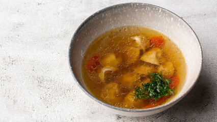 Tasty chicken soup bouillon with dumplings, chicken meat and parsley in a white bowl. Isolated on marble background. Healthy meal menu.