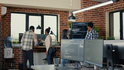 System developers analyzing code on wall screen tv looking for errors while team of coders...